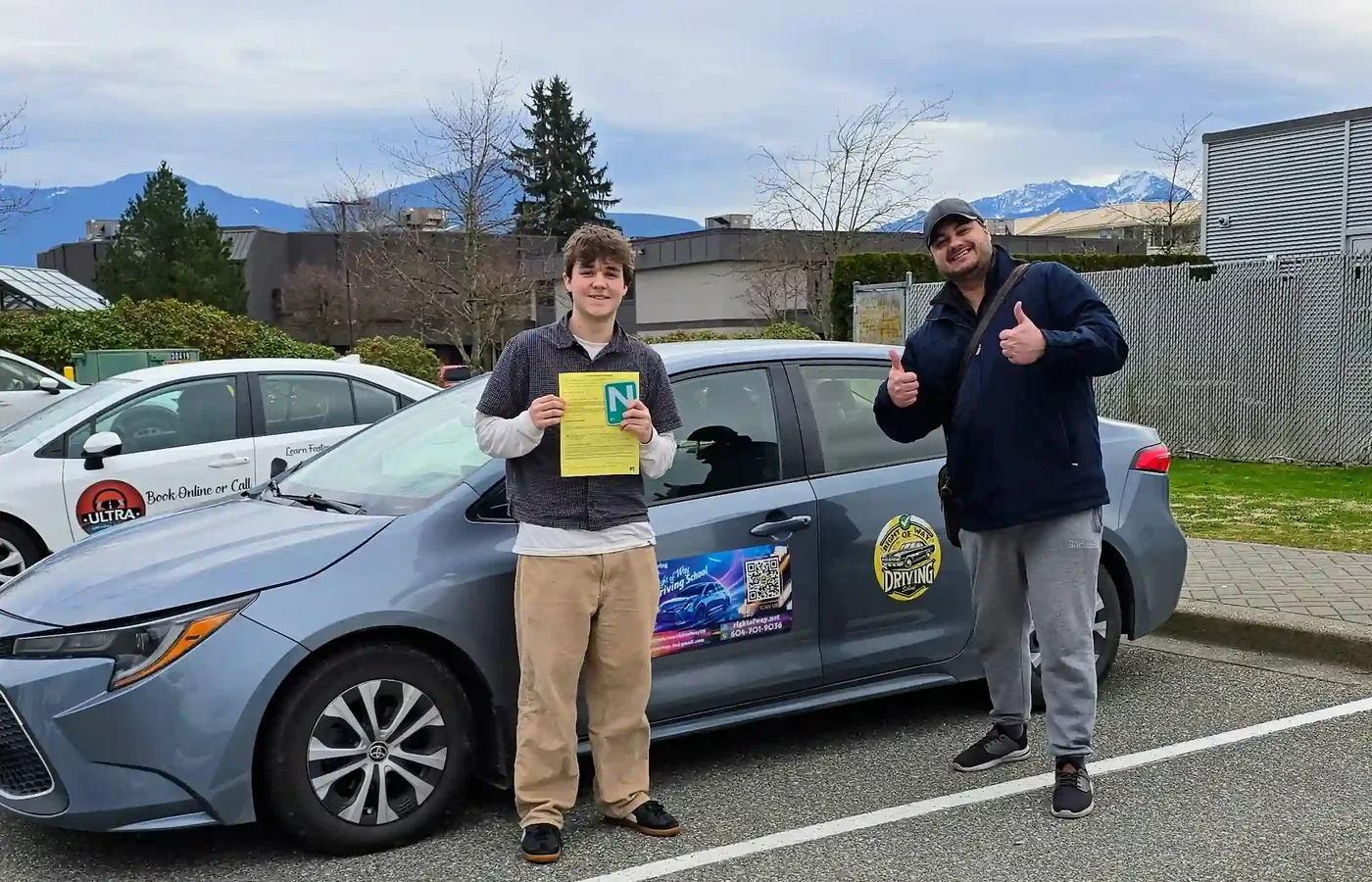 Teen student holding his road test result beside the training car with his instructor